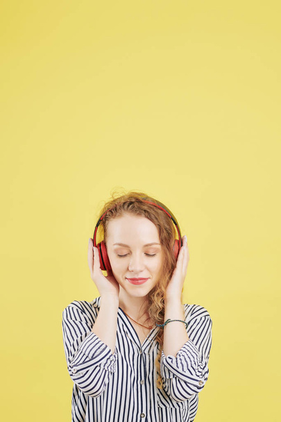 Mooie jonge vrouw sluit haar ogen en geniet van het luisteren naar meditatie en omgevingsgeluiden via applicatie om stress en kalme angst te beheren - Foto, afbeelding