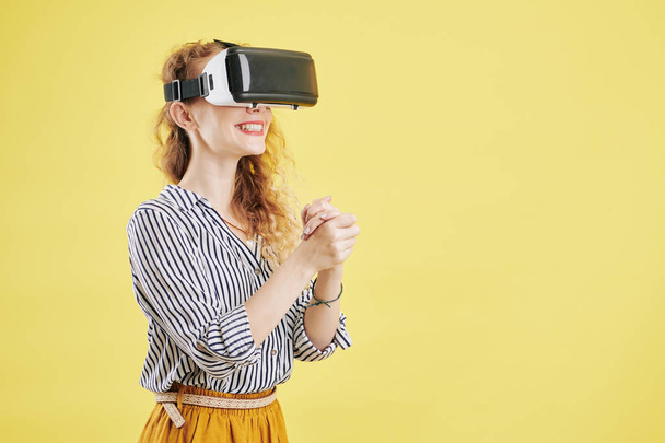 Portret van opgewonden jonge vrouw in headset genieten van het ervaren van virtual reality voor de eerste keer, geïsoleerd op geel - Foto, afbeelding