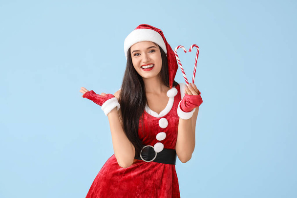 Beautiful young woman in Santa Claus costume and with candy canes on light background - Фото, зображення