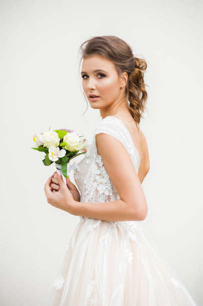 Giovane donna elegante con bouquet da sposa in un abito bianco lungo leggero che cammina vicino alla casa bianca prima della cerimonia nuziale
. - Foto, immagini