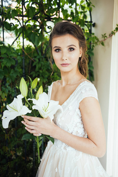 Mujer elegante joven con ramo de boda en un vestido blanco largo ligero caminando cerca de la casa blanca antes de la ceremonia de boda
. - Foto, Imagen