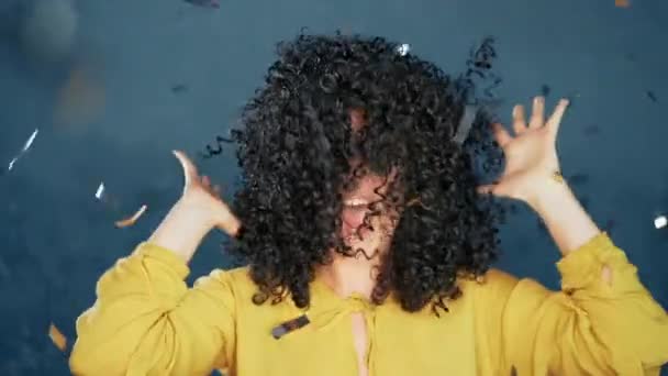 Surprised excited girl with curly hair having fun in confetti rain on blue background. Woman celebrating, depicts joy and happiness. Success, victory, holiday concept. - Video