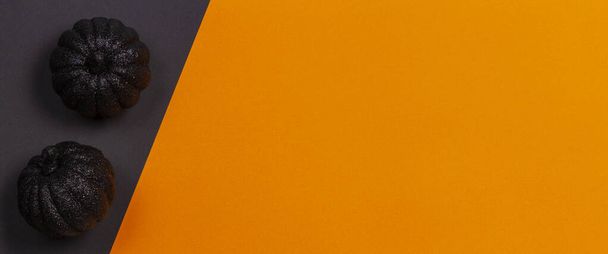 Minimální halloweenské pozadí. Dekorativní černé lesklé dýně na oranžovém a černém pozadí. Horní pohled - Fotografie, Obrázek