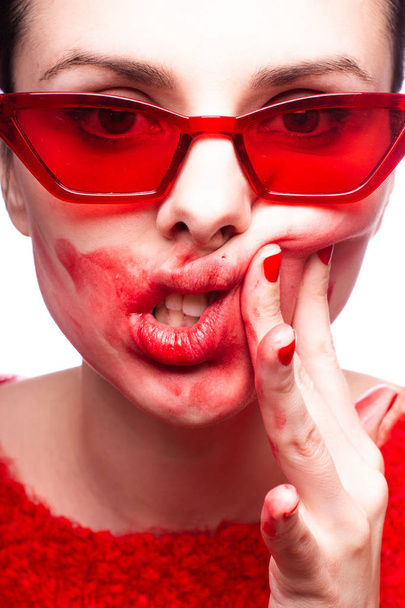 a girl in a red sweater and red glasses smears lipstick on her face - Photo, Image