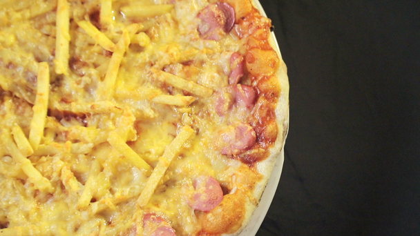 pizza close-up avec fromage et saucisse qui tourne autour de lui sur un fond noir vue du haut
 - Séquence, vidéo
