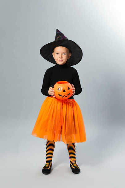 Cute little girl with pumpkin candy bucket wearing Halloween costume on grey background - Photo, image