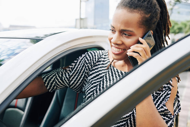 African young businesswoman talking on mobile phone while sitting in her car in the city - Fotografie, Obrázek