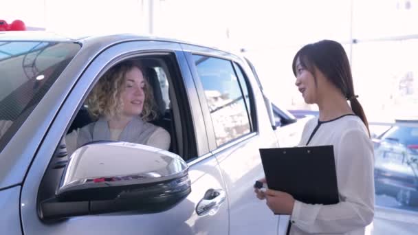 portret pracownika warsztat samochodowy z dziewczyną konsument, który pokazuje klucze wewnątrz samochodu podczas zakupu samochodu w salonie - Materiał filmowy, wideo