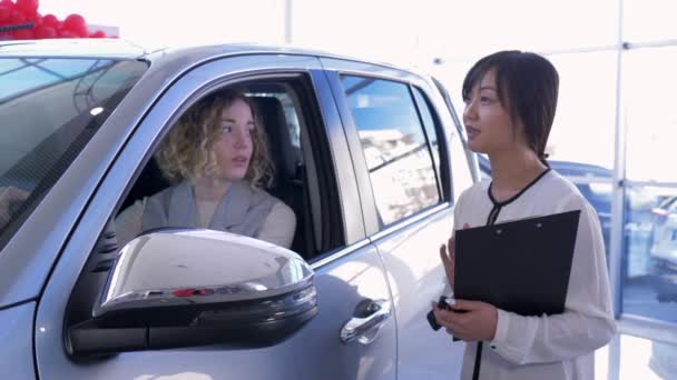 Portret profesjonalnego sprzedawcy samochodów przekazuje klucze klientce wewnątrz pojazdu podczas zakupu samochodu w salonie - Materiał filmowy, wideo