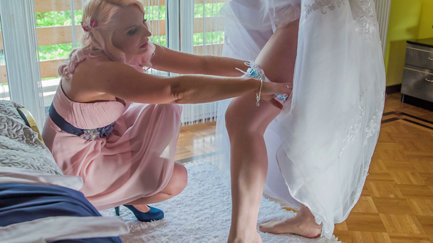 La damigella sta mettendo la giarrettiera sulla coscia della sposa. Lei la sta aiutando a vestirsi per il suo matrimonio
. - Filmati, video