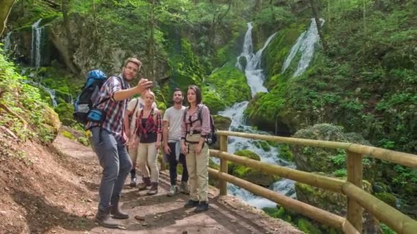 Un grupo de cinco amigos se está tomando una selfie juntos frente a una hermosa cascada. La naturaleza es excepcional en esta época del año
. - Metraje, vídeo