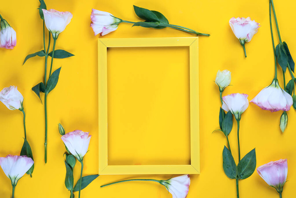 Empty yellow frame and flowers eustoma as layer on yellow paper background with copy space. Holiday concept - Foto, Imagem