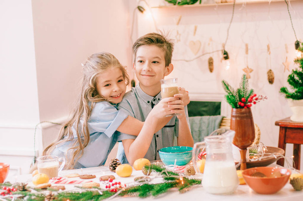 Cute little sister with long hair and an older brother drink cocoa and eat gingerbread cookies  in anticipation of Christmas. Christmas mood - Фото, зображення