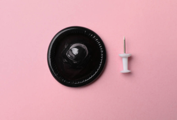 Black condom and pin on pink background, flat lay - Fotoğraf, Görsel