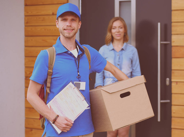 Smiling delivery man in blue uniform delivering parcel box to recipient - courier service concept. Smiling delivery man in blue uniform - 写真・画像