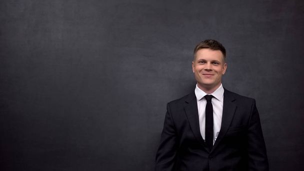 Positive businessman looking at camera, standing against black background, ad - Foto, Bild