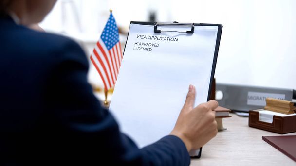Immigration officer approving visa application, american flag on table, tourism - Фото, изображение