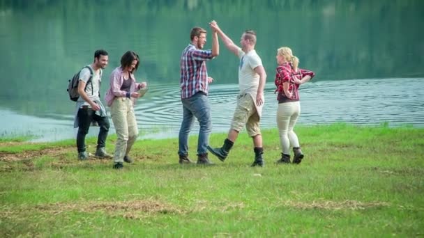 Группа молодых людей действительно расслабляется у озера. Они смеются и дают друг другу пять
. - Кадры, видео