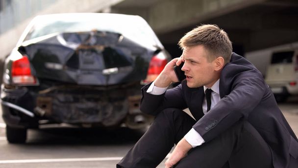 Worried man talking on phone outdoors broken auto background, traffic collision - Fotó, kép