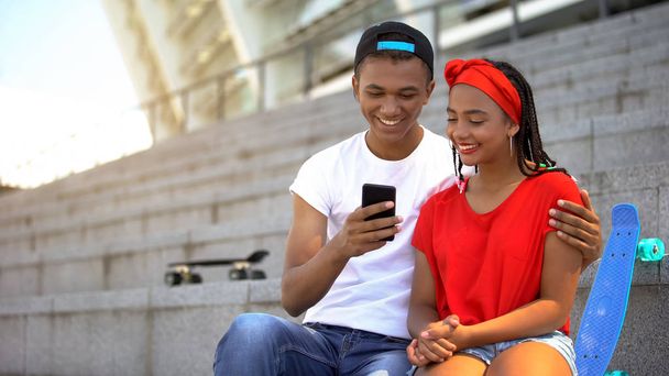 Smiling teenagers watching funny video on smartphone, spending leisure time - Fotó, kép