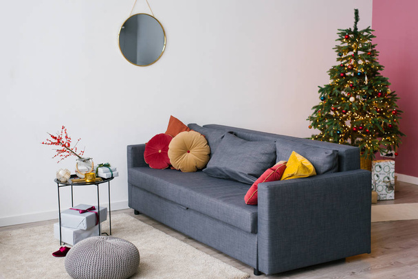 Ciemnoszara sofa z jasnoczerwonymi i żółtymi poduszkami, choinka we wnętrzu salonu w domu - Zdjęcie, obraz