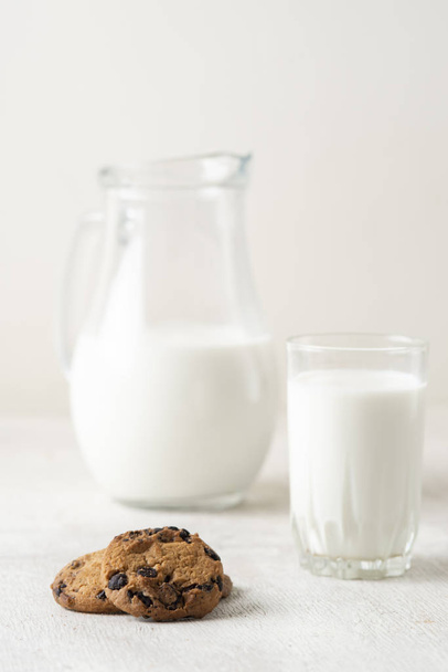 chocolate chip cookies and milk in a jug and a glass on a white wooden  background - Foto, Imagen