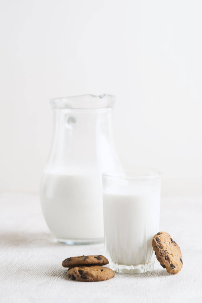 Milk in a jug and chocolate chip cookies on on a white wooden background copy space. - Foto, Imagen