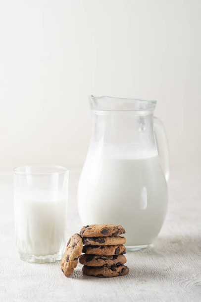 chocolate chip cookies and milk in a jug and a glass on a white wooden  background - Foto, imagen
