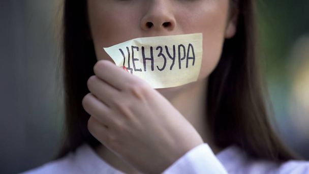 Woman resolutely taking off tape with censored word in russian over mouth - Fotó, kép