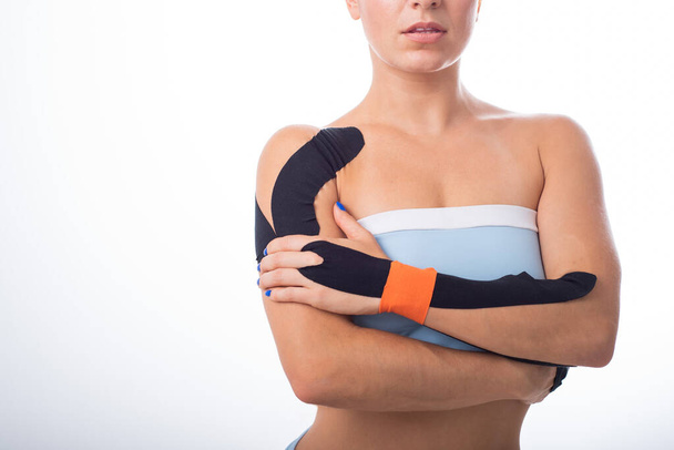 Female shoulder with kineziotape on a white background. Alternative medicine for sports injuries of joints and ligaments. Young sportswoman with medical record on a sore shoulder and wrist. - Fotó, kép