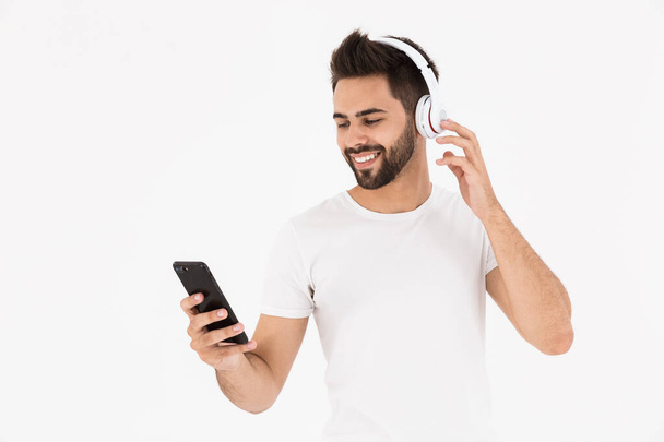 Image of unshaven smiling man listening music on cellphone and headphones - 写真・画像