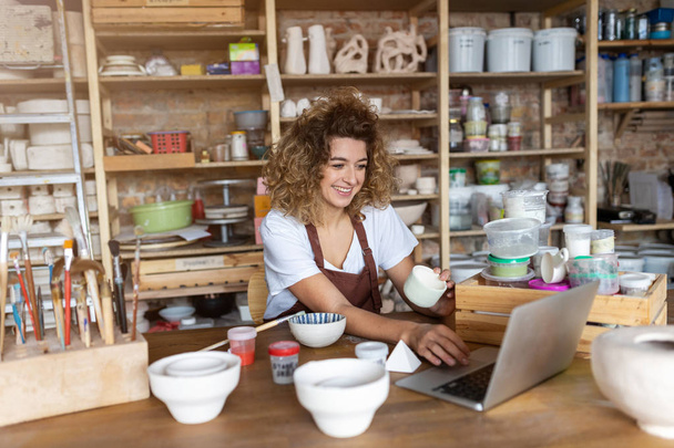 Woman pottery artist using laptop in art studio  - Photo, Image