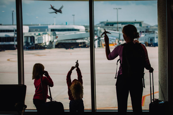 madre con niños juegan aviones de juguete en el aeropuerto, familia con equipaje esperando
 - Foto, imagen
