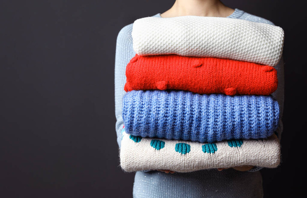 Woman holding pile of winter sweaters on dark background, closeup view. Space for text - Zdjęcie, obraz
