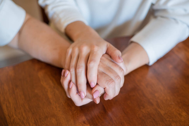 Idős anya és lánya kéz a kézben ülnek az asztalnál.Közelkép a nők különböző generációk fogják egymás kezét. Közelkép az anyáról és a lányokról Kéz a kézben - Fotó, kép