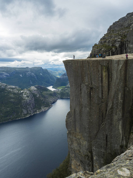 Profile view of famous Preikestolen massive cliff at fjord Lysefjord, famous Norway viewpoint with group of tourists and hikers. Moody autumn day. Nature and travel background, vacation and hiking - Photo, Image