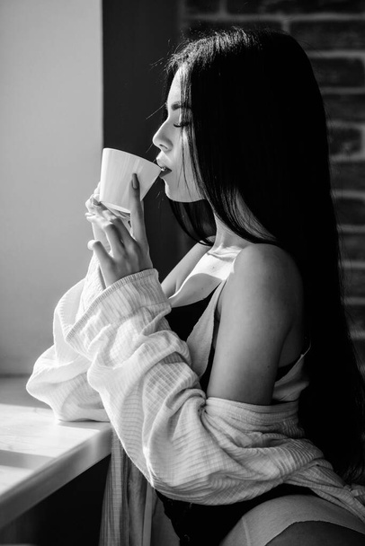 The best coffee for her daily routine. Sensual girl drinking her favorite morning coffee. Pretty woman drinking fresh hot coffee at window. Sexy girl holding ceramic coffee cup - Foto, afbeelding