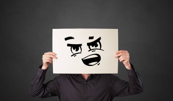 Persona sosteniendo un papel con divertido emoticono delante de su cara
 - Foto, Imagen