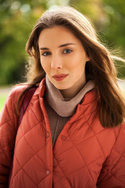 Young stylish woman in a salmon down jacket posing on a backgrou - Valokuva, kuva
