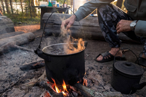 Man kookt in bowlers boven een vuur in het bos. - Foto, afbeelding