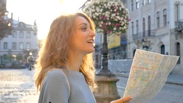 glücklich aufgeregtes erwachsenes Mädchen blickt auf die Papierkarte und sucht frühmorgens in der antiken europäischen Stadt auf dem leeren Platz nach Orientierung - Filmmaterial, Video