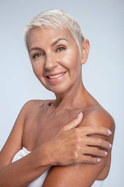 Beautiful tanned and smiling lady hugging herself - Фото, изображение