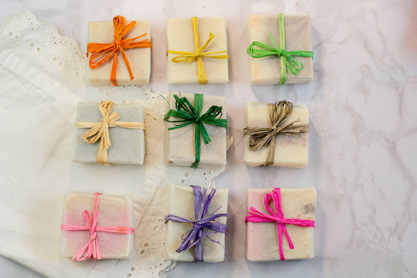 handmade organic craft soap in gift wax wrapping  paper with multi colored eco raffia ribbons on marble surface with space for text. Present gift soap flat lay top view2 - Foto, Imagen