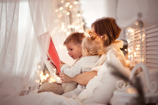 Mamá lee un libro para los niños en una acogedora noche de invierno
 - Foto, imagen