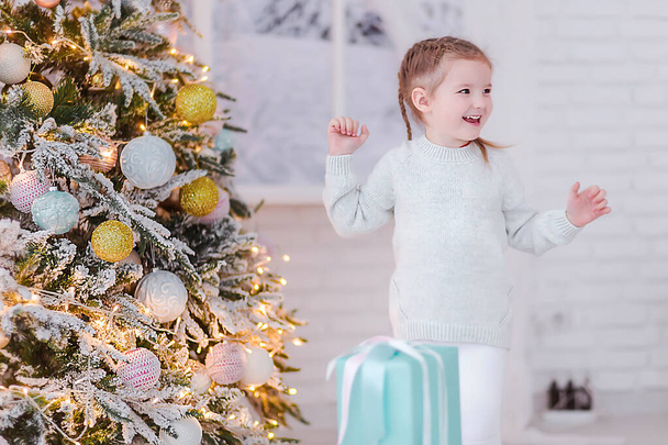 Happy little girl near the Christmas tree and New Years gift - Foto, afbeelding