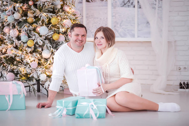 Одружена пара сидить серед подарунків біля новорічної ялинки
 - Фото, зображення