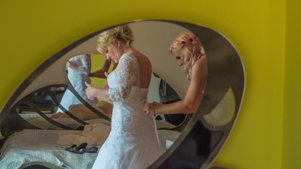 The bridesmaid is helping the bride get dressed for her wedding day. We can see them in the mirror. - Footage, Video