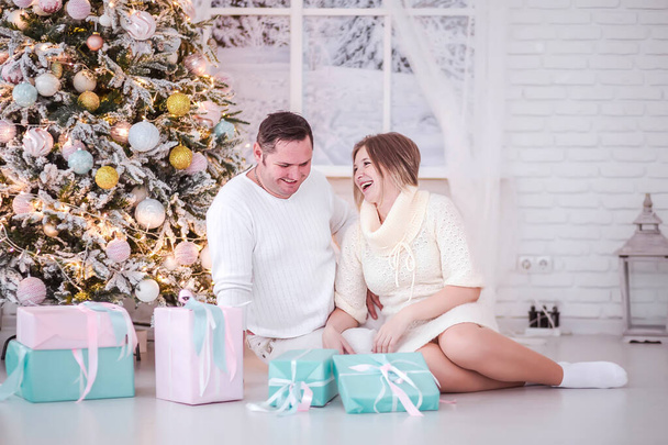 Супружеская пара сидит среди подарков возле новогодней елки
 - Фото, изображение