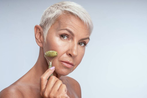 Close up of a pretty and healthy lady using jade roller on a side of her face - Foto, Bild