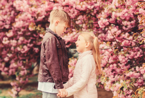 Kids in love pink cherry blossom. Love is in the air. Couple adorable lovely kids walk sakura garden. Tender love feelings. Little girl and boy. Romantic date in park. Spring time to fall in love - Photo, Image
